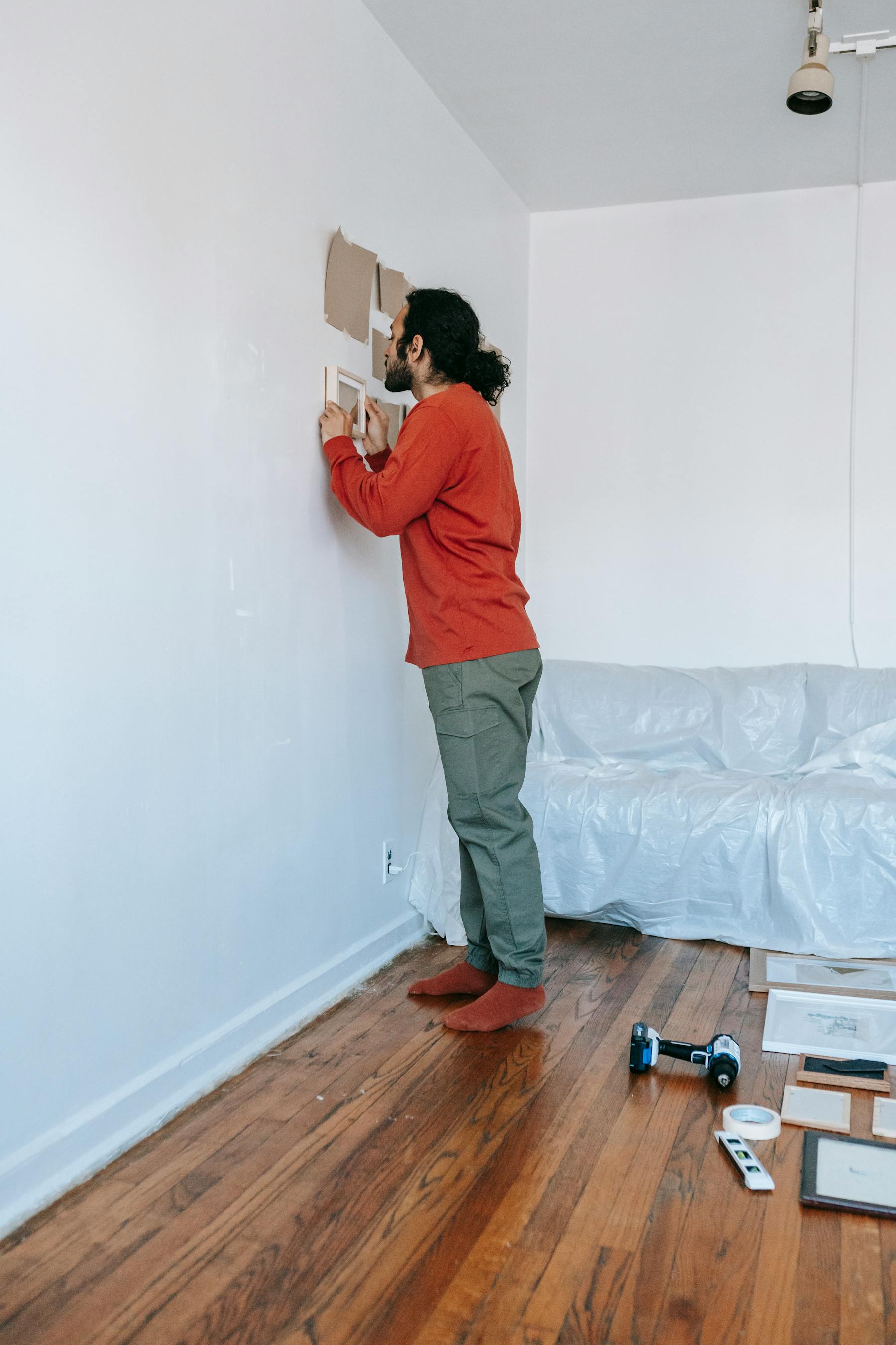 People measuring and hanging a framed picture on a wall